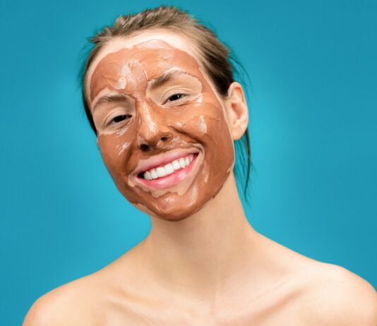 Domowa maseczka na twarz w kolorze brązowym. Usmiechnięta kobieta ze spiętymi, brązowymi włosami i maseczką na twarzy.