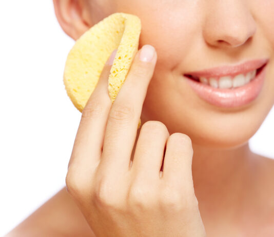Domowy peeling – jak przygotować go samodzielnie? Młoda kobieta trzymająca w dłoni okrągłą żółtą gąbkę i lekko uśmiechnięta
