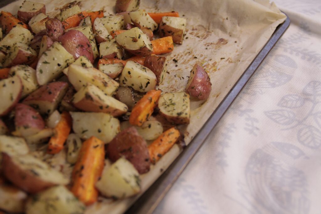 Zdrowe przekąski w postaci warzywnych frytek. Na blasze do pieczenia leżą marchewka i ziemniaki pokrojone w talarki i obsypane przyprawami.