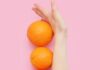 Kobieca ręka odgradzająca pomarańczowe, na różowym tle. Ilustracja dotycząca tego, jak fruktoza wpływa na utrzymanie prawidłowej wagi.
