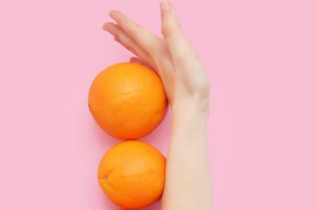 Kobieca ręka odgradzająca pomarańczowe, na różowym tle. Ilustracja dotycząca tego, jak fruktoza wpływa na utrzymanie prawidłowej wagi.