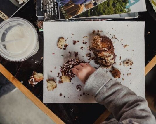 Czym zastąpić słodycze w diecie dziecka? Dziecięca rączka sięgająca po słodycze leżące na stole. Jeśli zastanawiasz się, czym zastąpić słodycze w diecie dziecka, zacznij od wprowadzania owoców.