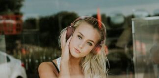 Młoda dziewczyna o blond włosach, która ma na głowie duże słuchawki. Zdjęcie zrobione przez szybę. Ilustracja artykułu o tym, jaka powinna być muzyka do pracy.