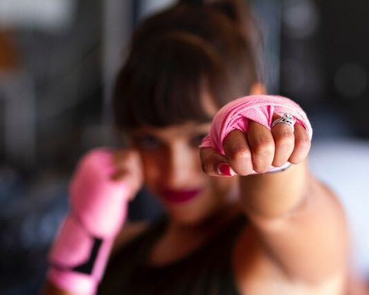 Trening obowodowy to dobry sposób na to, jak pozostac w formie, nawet kiedy nie można skorzystać z siłowni. Na zdjęciu dziewczyna w różowych rękawiczkach do trningu ćwiczy wyprowadzanie ciosu.